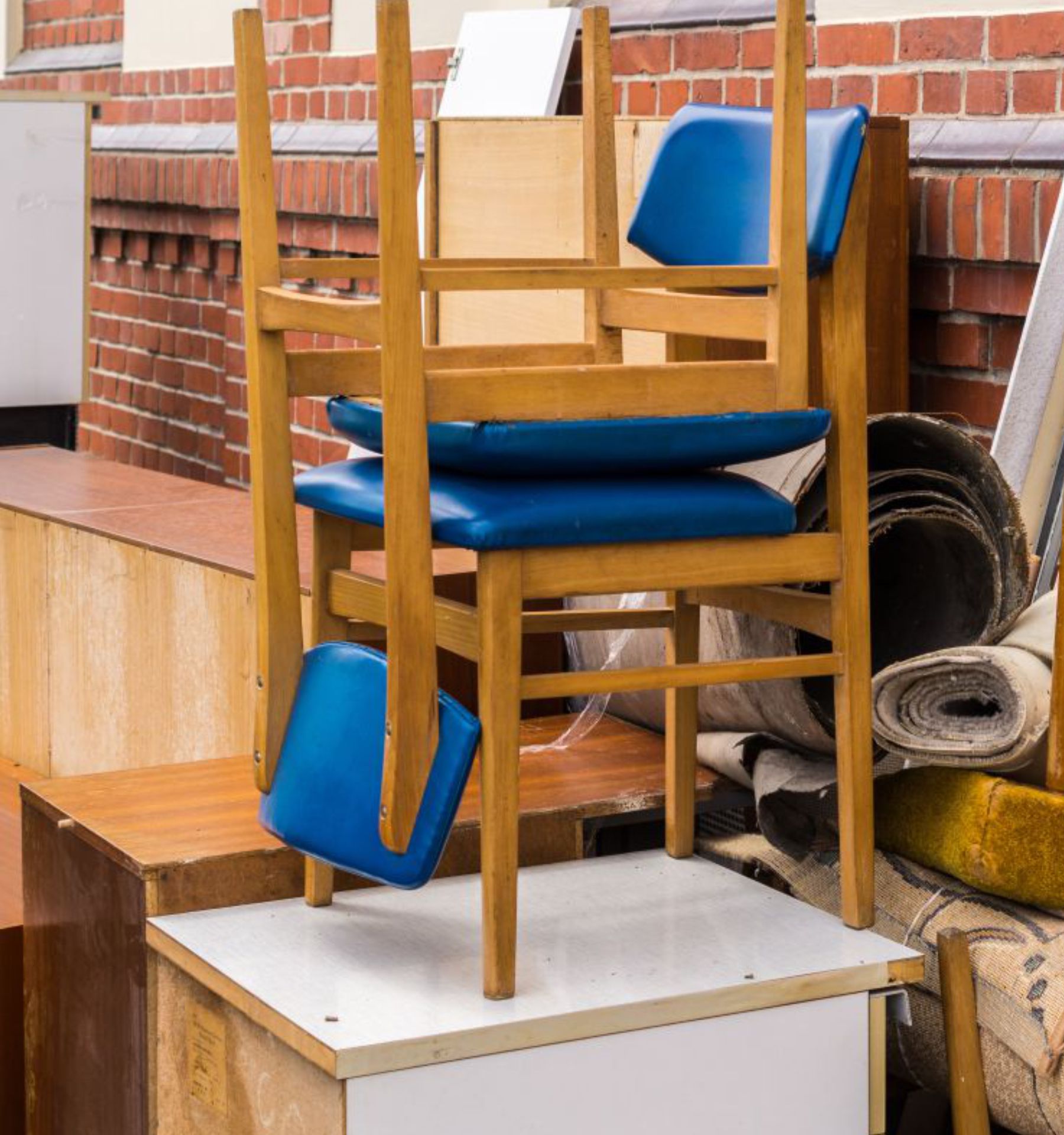 Das Bild zeigt einen großen Stapel aus alten Möbeln, Holzstühlen, Schränken und aufgerollten Teppichen vor einer roten Backsteinwand. Die ausrangierten Einrichtungsgegenstände stehen zur Abholung bereit und verdeutlichen den Umfang einer Entrümpelung oder Sperrmüllentsorgung.